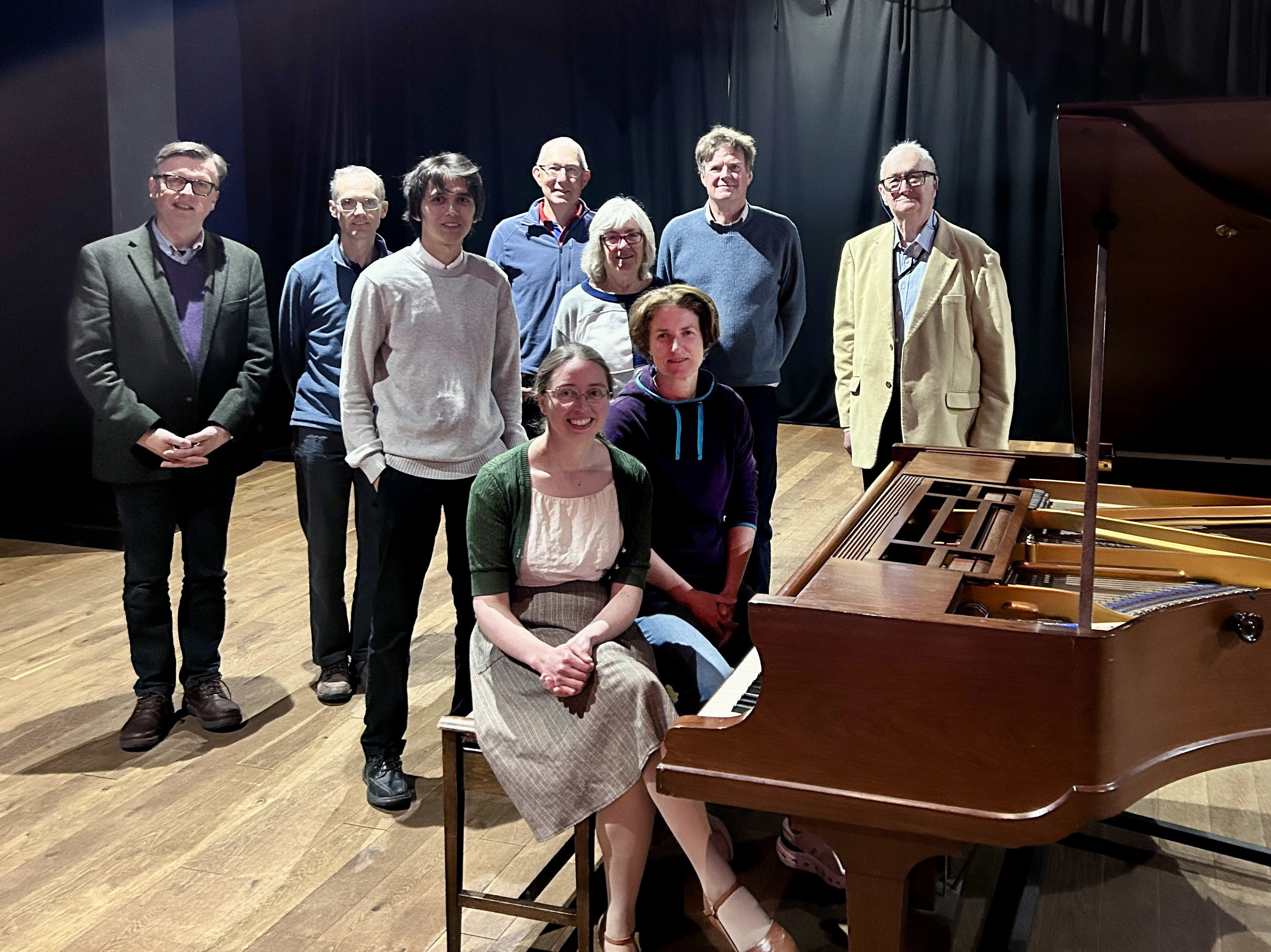 Members of the Exeter Piano Meetup Group standing around a grand piano in the Cygnet Theatre.
